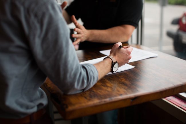 two men at a table for a meeting, hands outstretched